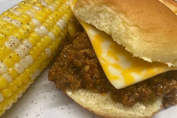 sloppy joe on a bun with an ear of corn